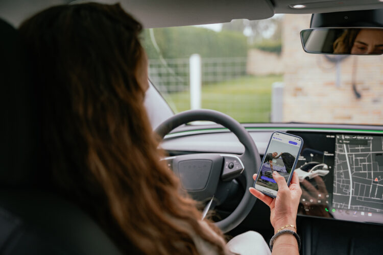 En person sidder i en bil og holder en smartphone, hvorpå der vises en mekaniker-app. Bilen har et moderne design med en detaljeret GPS-skærm i forruden.
