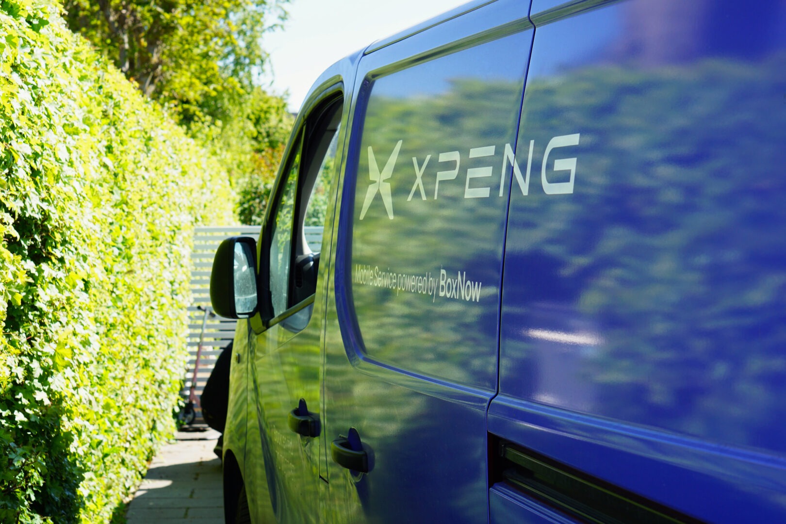 XPENG servicebil fra BoxNow parkeret ved en grøn hæk klar til mobil elbilservice