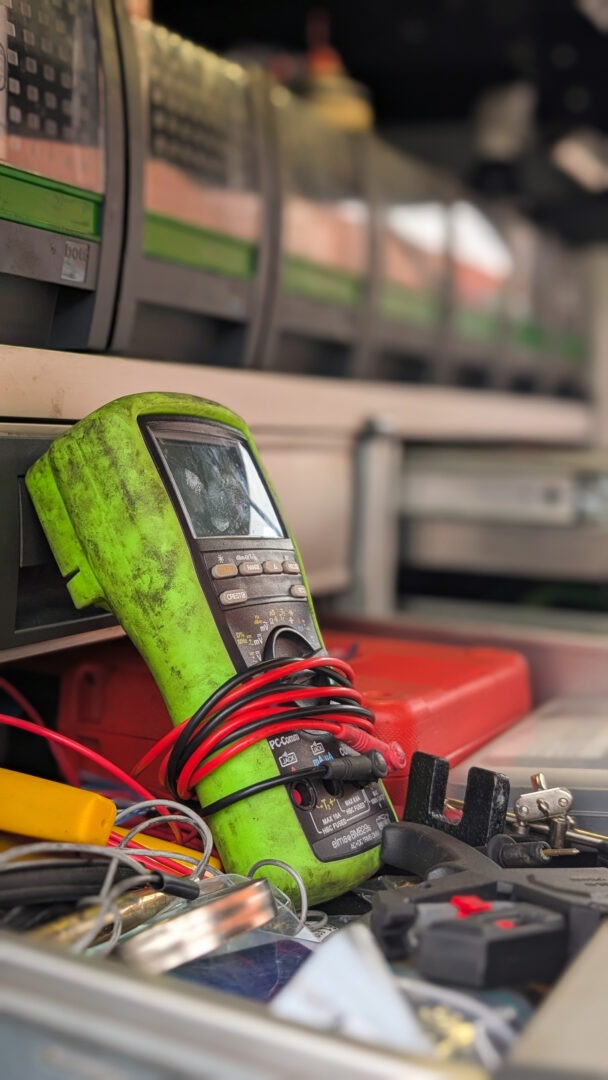 Multimeter med slidte knapper og røde ledninger i værkstedsbilens skuffe.
